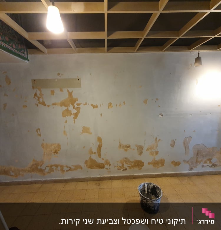 קיר עם קילופי צבע ודלי צבע על הרצפה